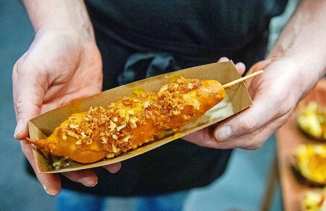 Der fertig ausgebackene Cheesy Corndog wird mit Rstzwiebeln getoppt.  | Foto: Bernd Diekjobst (dpa)