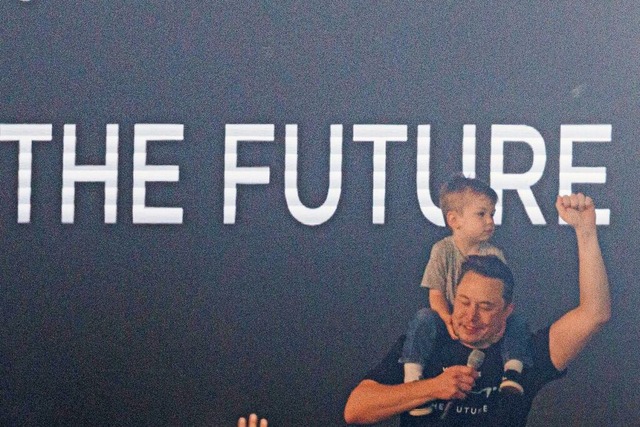 Tesla-Chef Elon Musk spricht in der Te...rgt dabei ein Kind auf den Schultern.  | Foto: Carsten Koall (dpa)