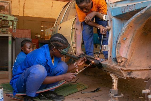 Wie in einer Kfz-Werkstatt in Burkina Faso Frauen an Motorrdern schweien und schrauben