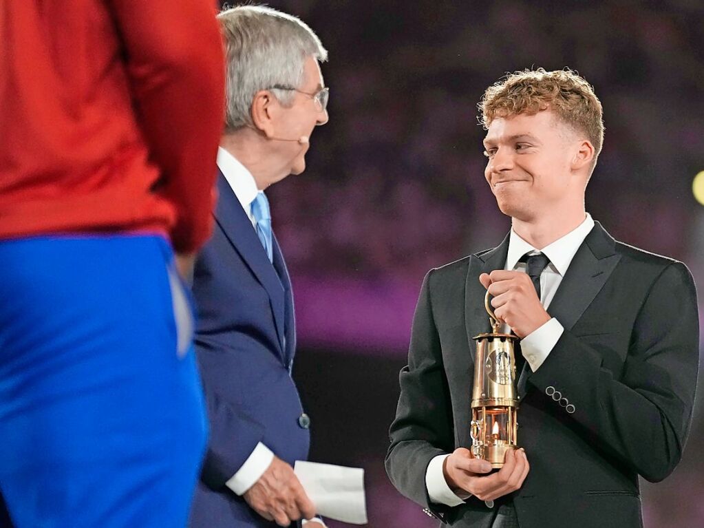 Der franzsische Schwimmer Leon Marchand trgt eine Laterne mit der olympischen Flamme zusammen mit IOC-Prsident Thomas Bach (l).