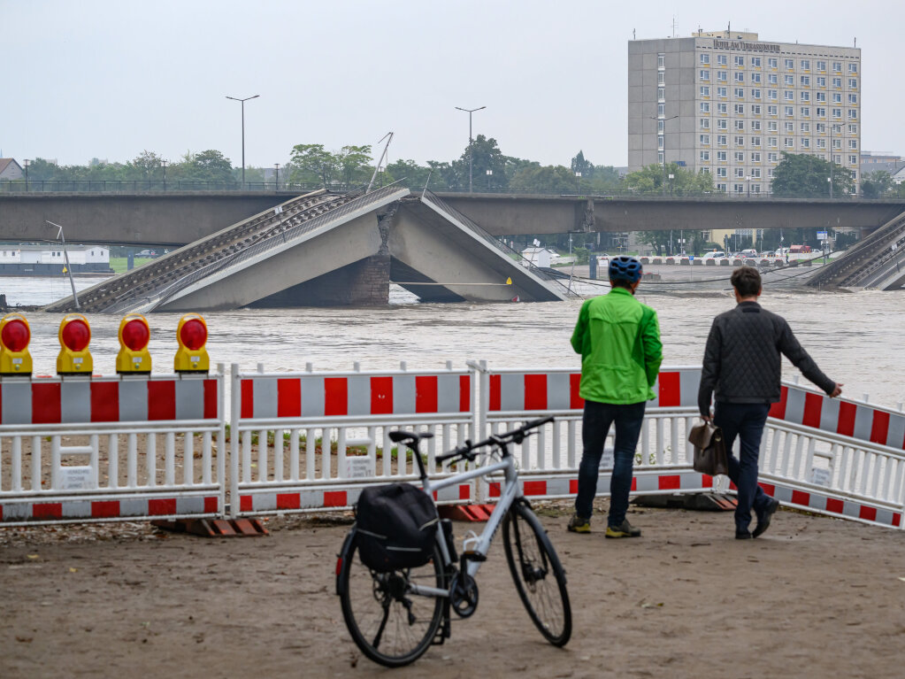 Dresden: Zwei Mnner stehen vor der vom Hochwasser der Elbe umsplten teileingestrzten Carolabrcke an einer Absperrung am Ufer.