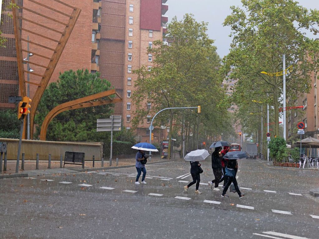 Barcelona: Menschen gehen mit Regenschirmen in strmendem Regen ber eine Strae.