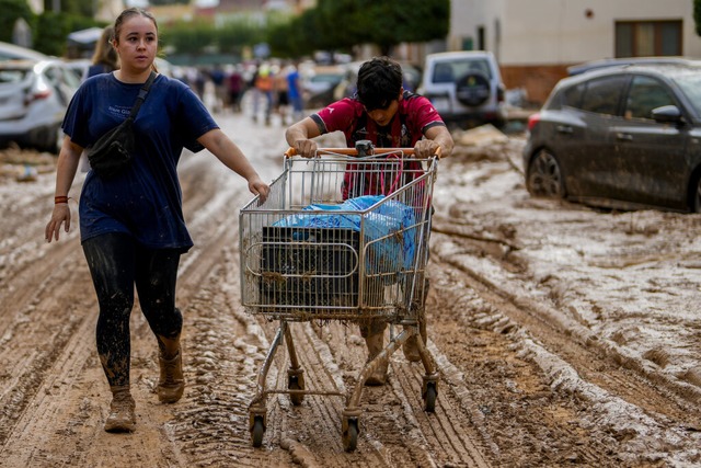 Zwei Personen schieben einen Einkaufsw...iten durch eine Strae voller Schlamm.  | Foto: Manu Fernandez (dpa)