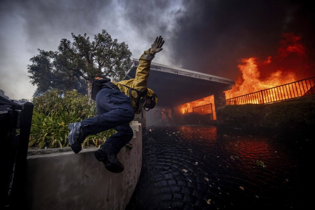 Ein Feuerwehrmann springt ber einen Zaun, whrend er das Feuer bekmpft.  | Foto: Ethan Swope (dpa)