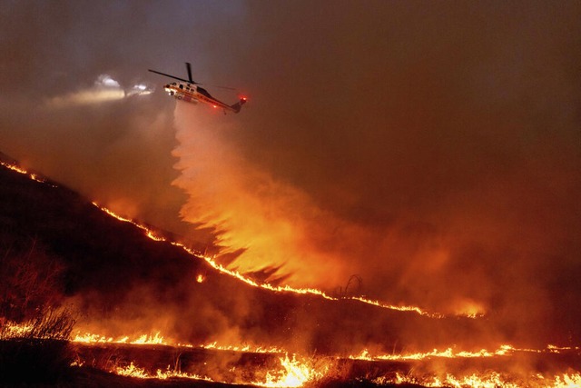 Ein Hubschrauber wirft Wasser auf das ...uer in den West Hills von Los Angeles.  | Foto: Ethan Swope (dpa)