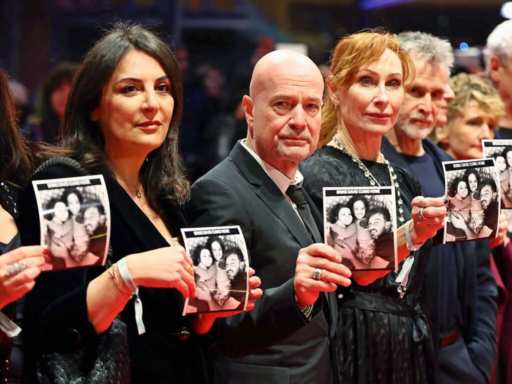 Menschenrechtsaktivistin Dzen Tekkal (l-r), Schauspieler Christian Berkel, Schauspielerin Andrea Sawatzki, Schauspieler Ulrich Matthes und Tricia Tuttle, Intendantin der Berlinale, stehen am Erffnungsabend der Berlinale auf dem Roten Teppich und halten Fotos der israelischen Geisel