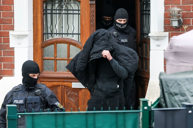 Polizeibeamte f&uuml;hren einen Tatver...l;chtigen aus einem durchsuchten Haus.  | Foto: Christoph Reichwein/dpa