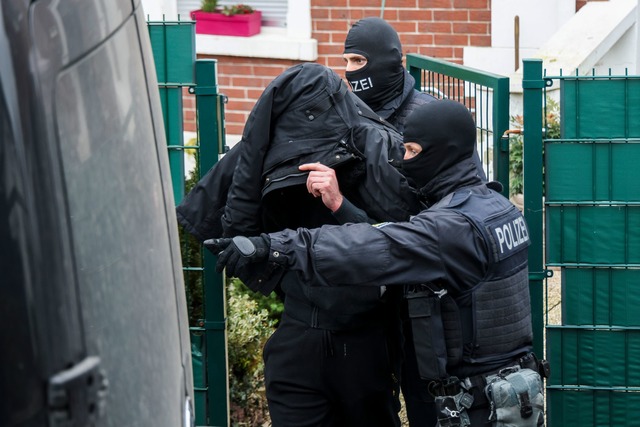 Polizeibeamte f&uuml;hren einen Tatver...l;chtigen aus einem durchsuchten Haus.  | Foto: Christoph Reichwein/dpa