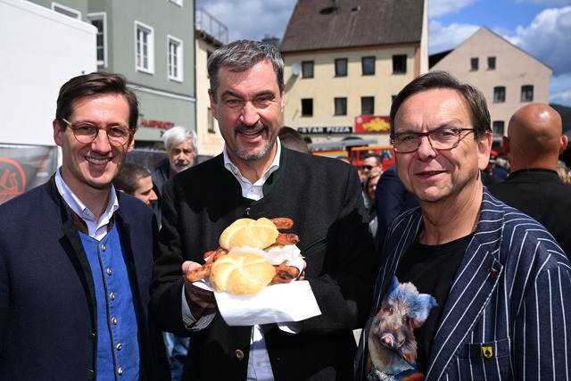 Markus S&ouml;der (M.) h&auml;lt Bratwurst-Semmeln in die Kamera.  | Foto: Felix H&ouml;rhager/dpa