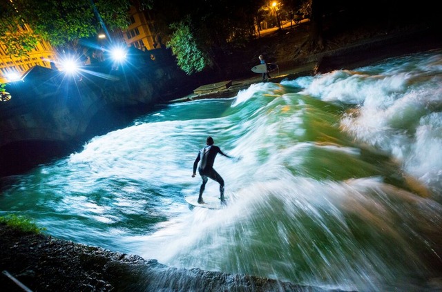 Ein Surfer reitet bei Nacht mit seinem...lle des Eisbachs im Englischen Garten.  | Foto: Peter Kneffel (dpa)